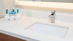 Ein Badezimmer mit einem weißen Waschbecken, einem Spiegel und Toilettenartikeln auf einem kleinen Tisch.