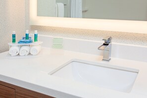 Ein Badezimmer mit einem weißen Waschbecken, einem Spiegel und Toilettenartikeln auf einem kleinen Tisch.