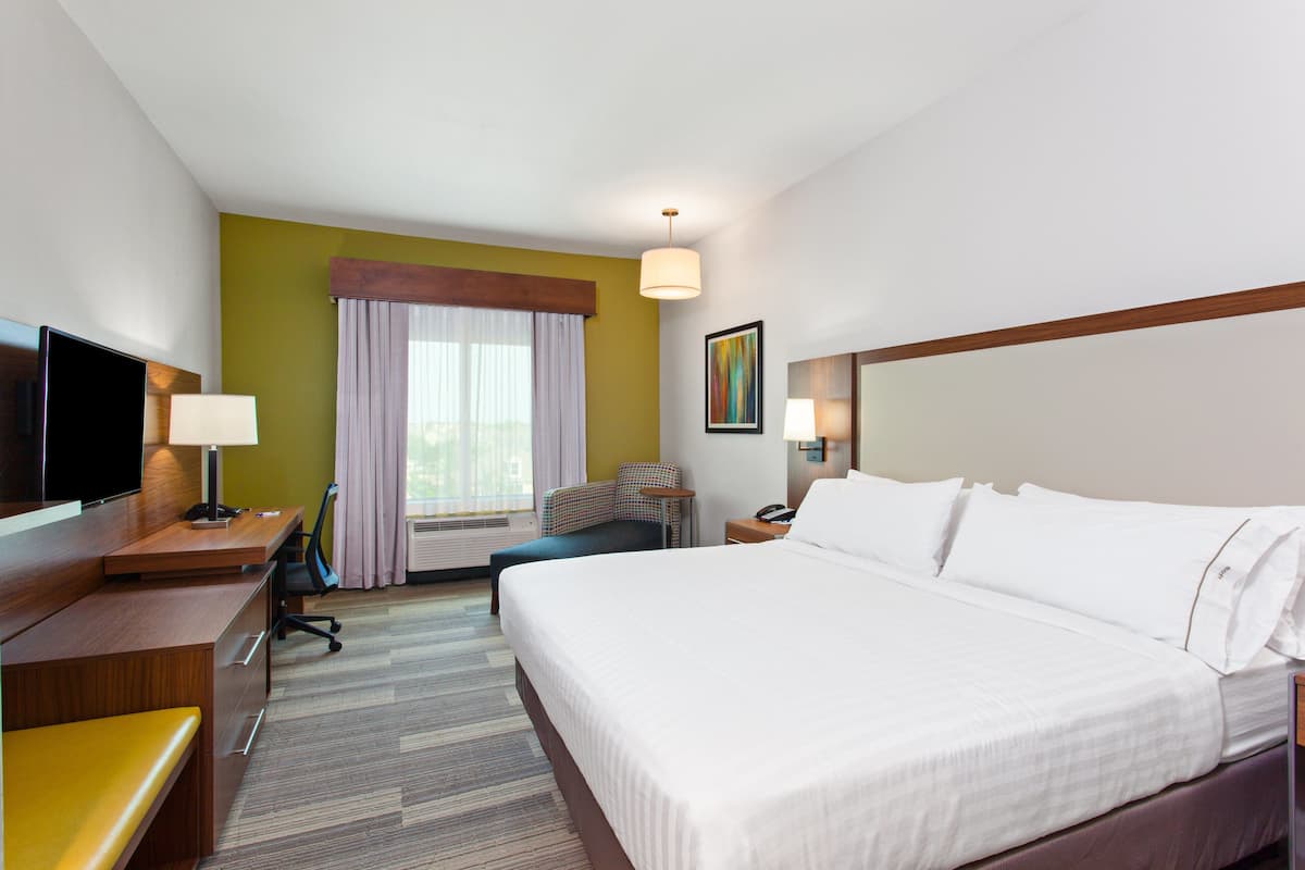 Hotelkamer met een groot bed, een bureau met een televisie, een stoel, een lamp en een raam met gordijnen.
