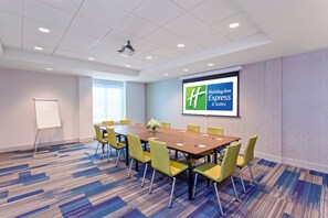 Een vergaderruimte met een lange tafel, gele stoelen, een projectiescherm en een whiteboard.