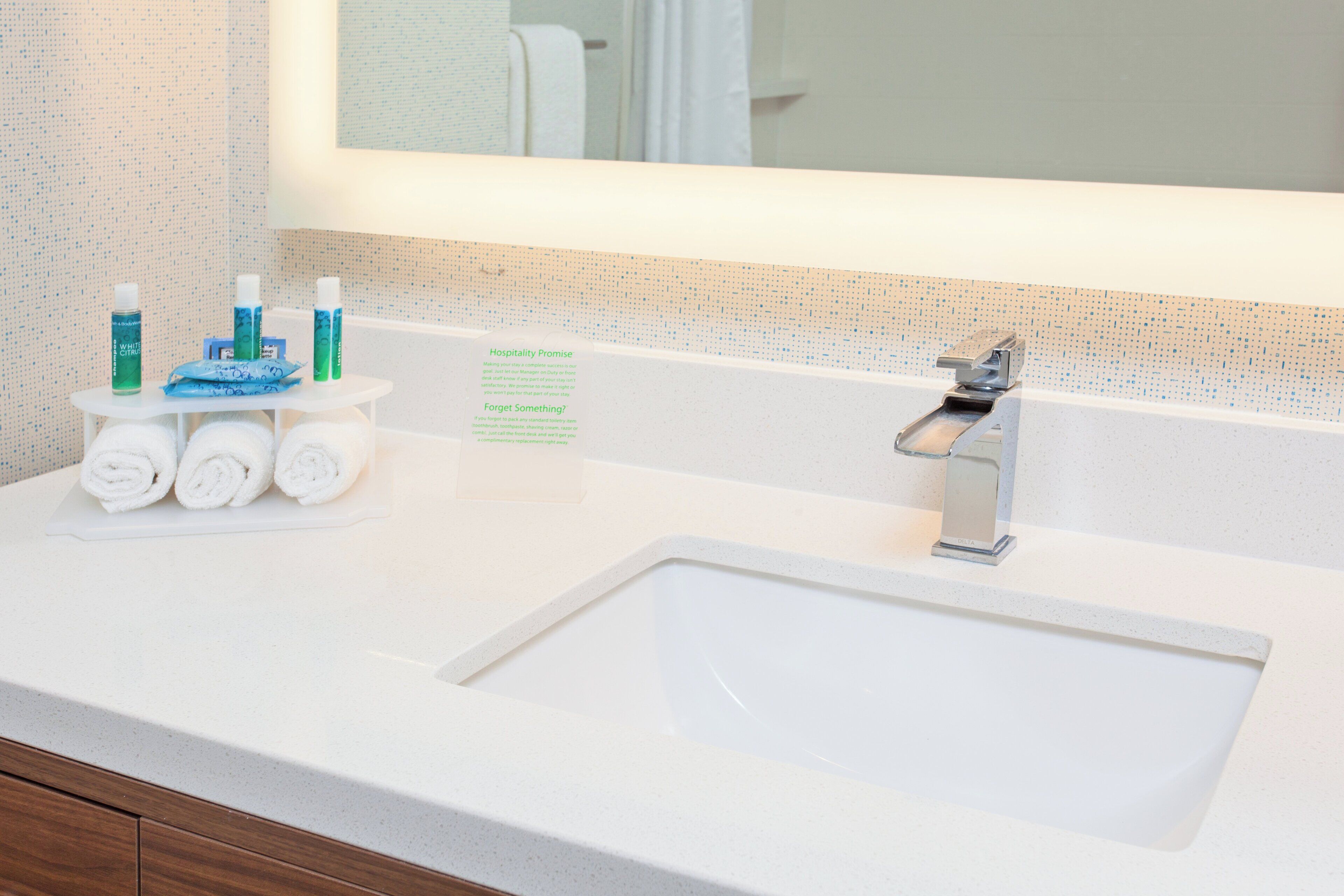 A hotel bathroom with a white sink, a mirror above it, and toiletries on a small table.