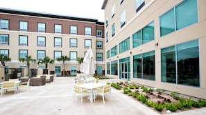 Une cour d’hôtel avec des espaces de détente en plein air, des palmiers et une façade de bâtiment moderne.