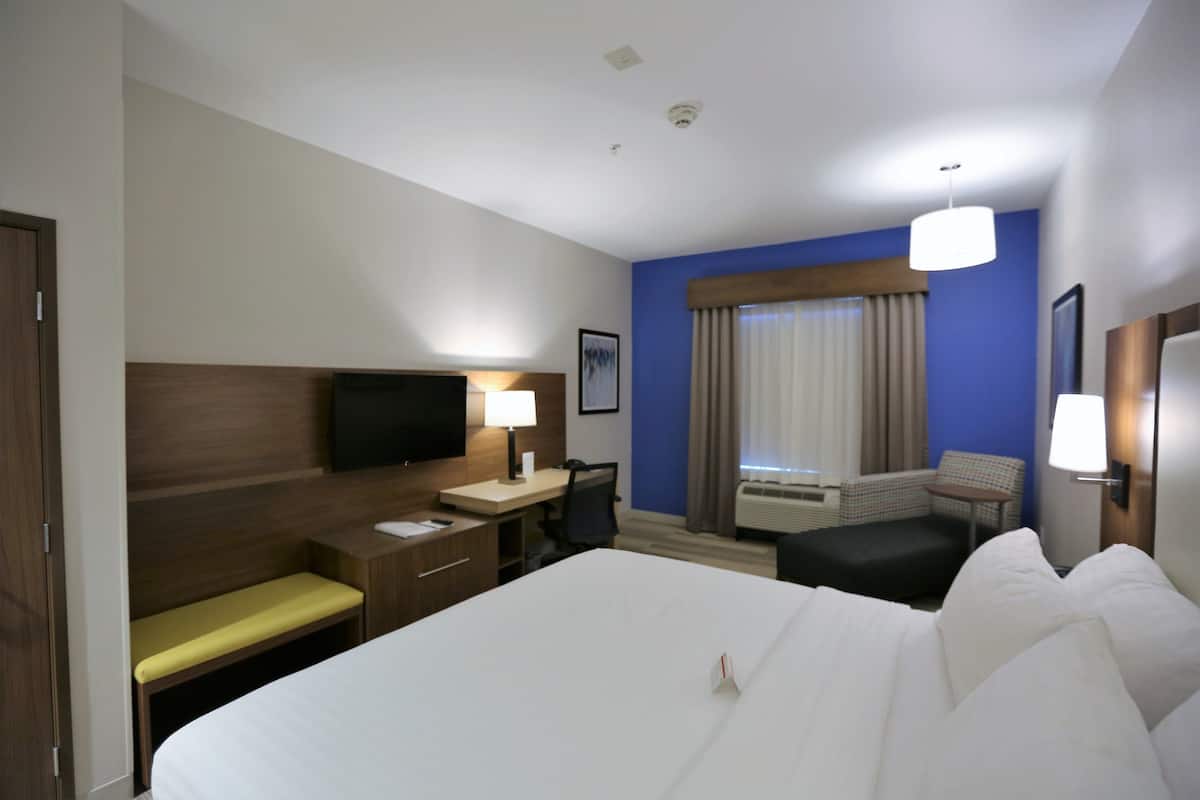 Een hotelkamer met een groot bed, een bureau met stoel, een televisie, een raam met gordijnen en een kleine tafel met stoel.