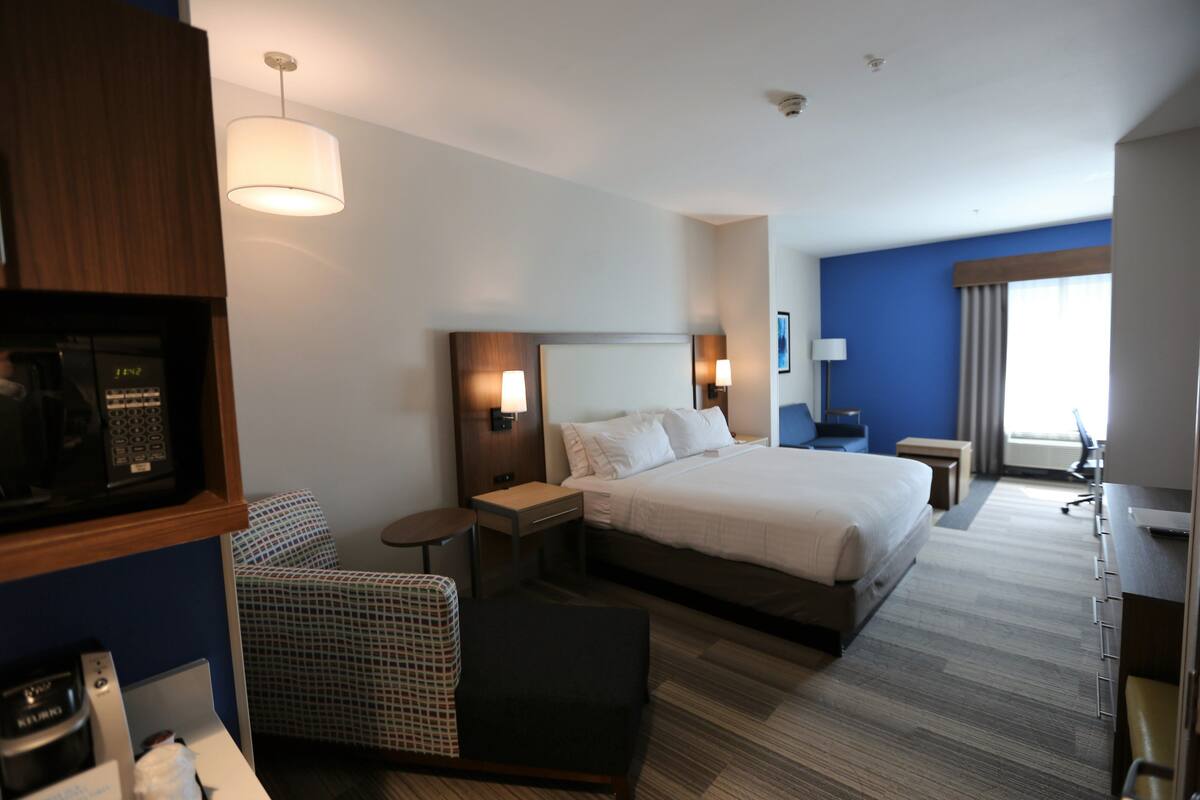 Een hotelkamer met een bed, nachtkastjes, een bureau, een stoel, een televisie en een raam met gordijnen.