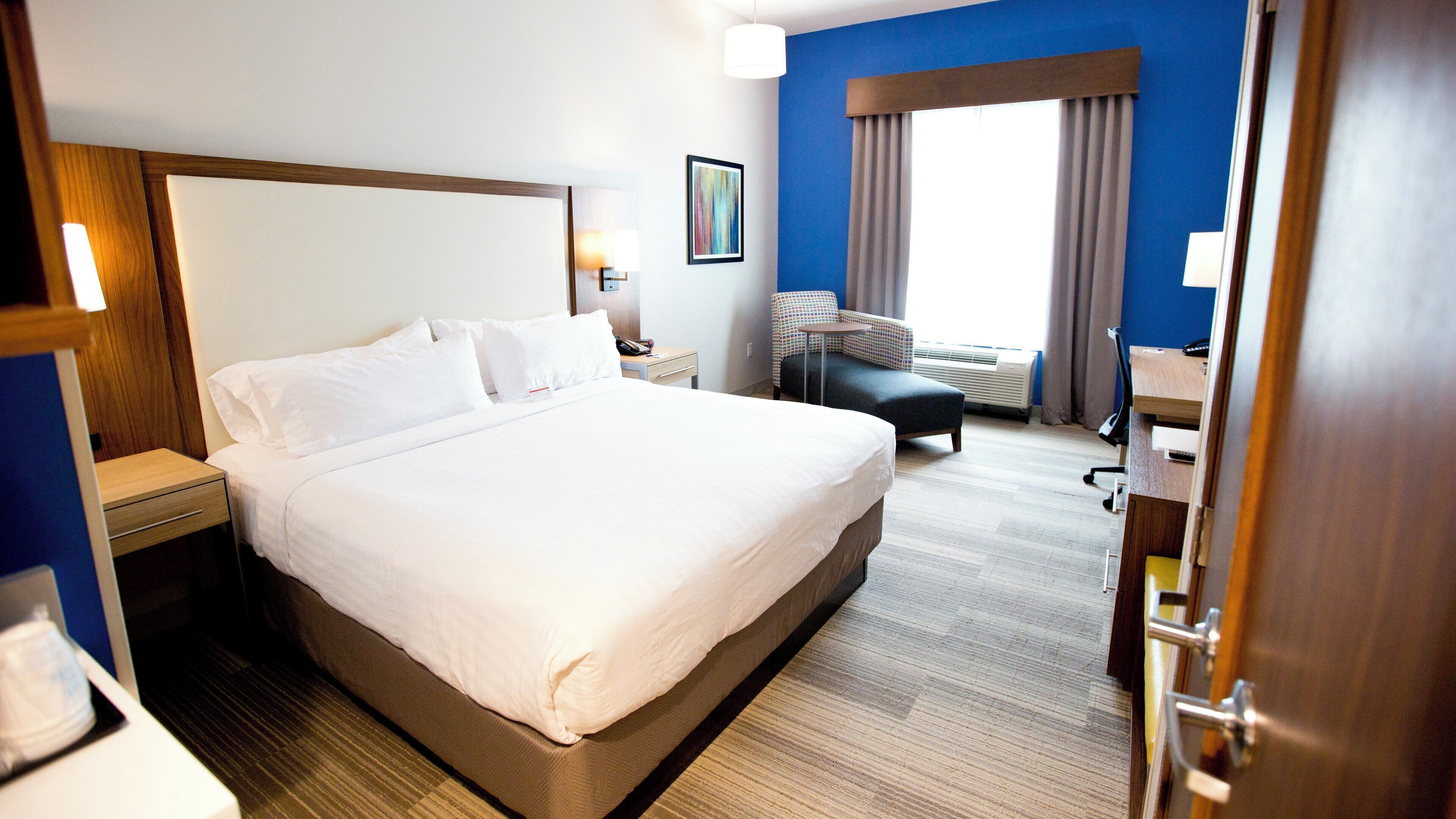 Ein Hotelzimmer mit einem großen Bett, einem Schreibtisch, einem Sessel, einem Nachttisch und einem Fenster mit Vorhängen.