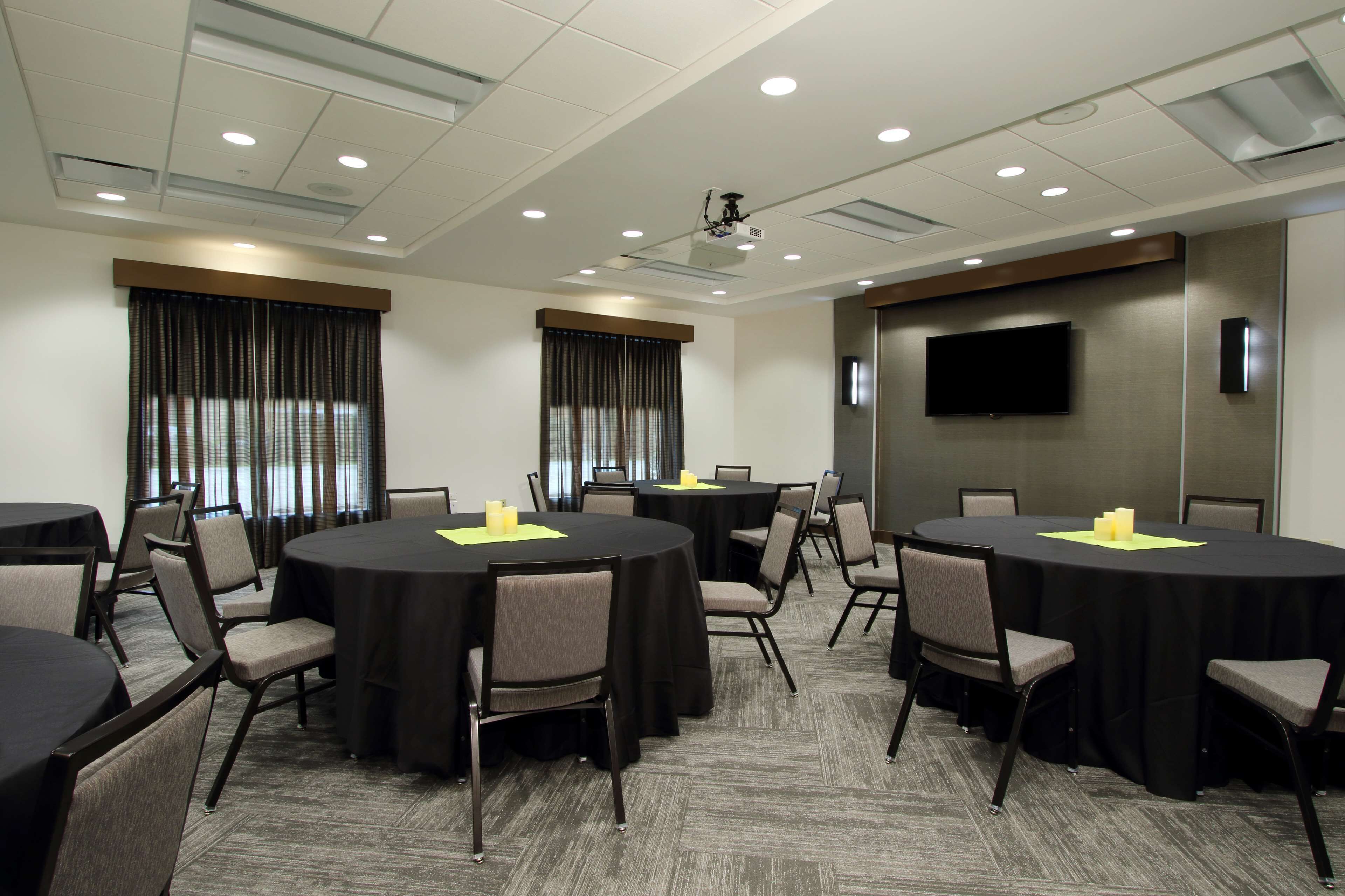 A conference room with round tables, chairs, a projector, and a TV screen.