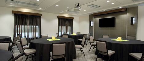 A conference room with round tables, chairs, a projector, and a TV screen.