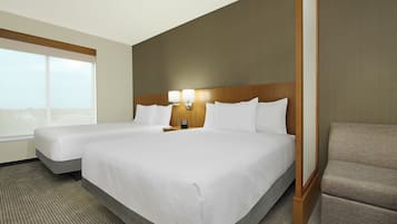 Hotellihuone, jossa on kaksi sänkyä, yöpöytä valaisimineen, näkymä kaupunkiin ja suuri ikkuna.