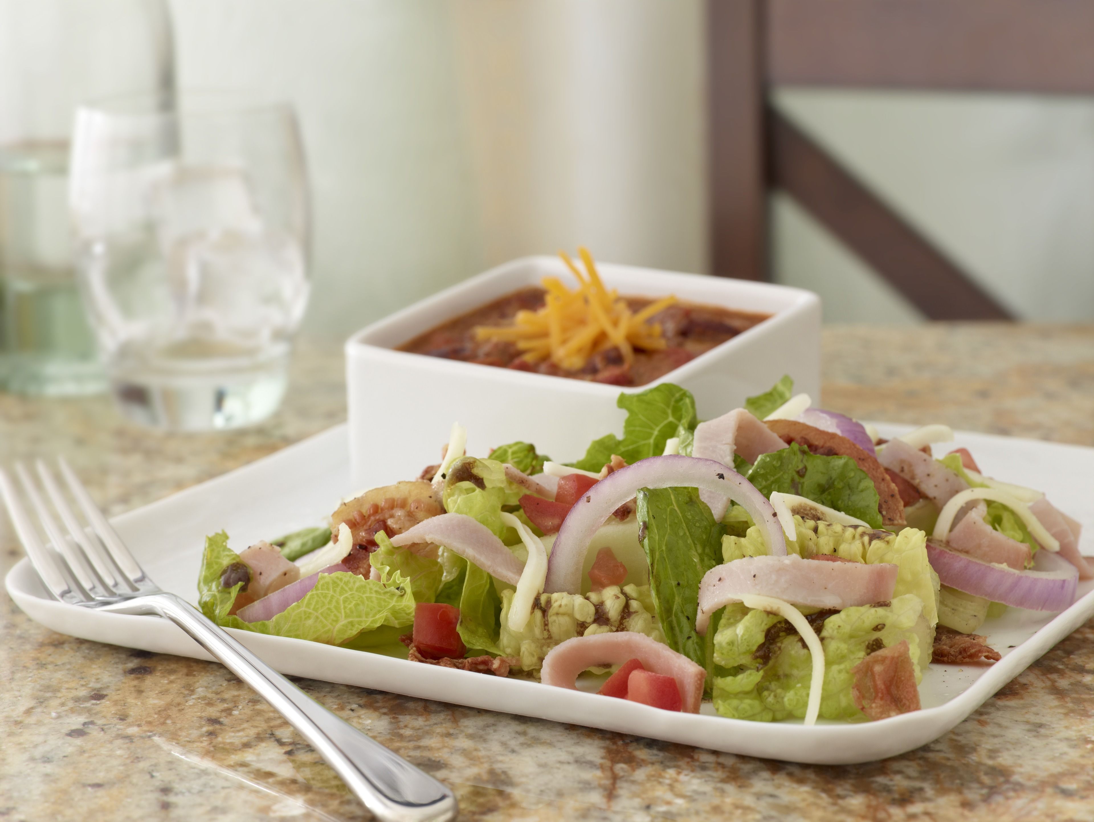A plate of salad with various ingredients and a bowl of soup in the background.