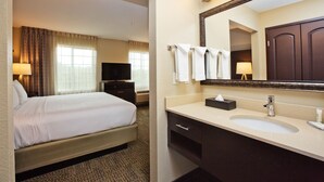 Quarto de hotel com cama, banheiro com pia, espelho e televisão.