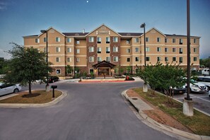A multi-story hotel with a central entrance, parking area, and a clear sky. - Staybridge Suites Austin South Interstate Hwy 35 by IHG (Austin)
