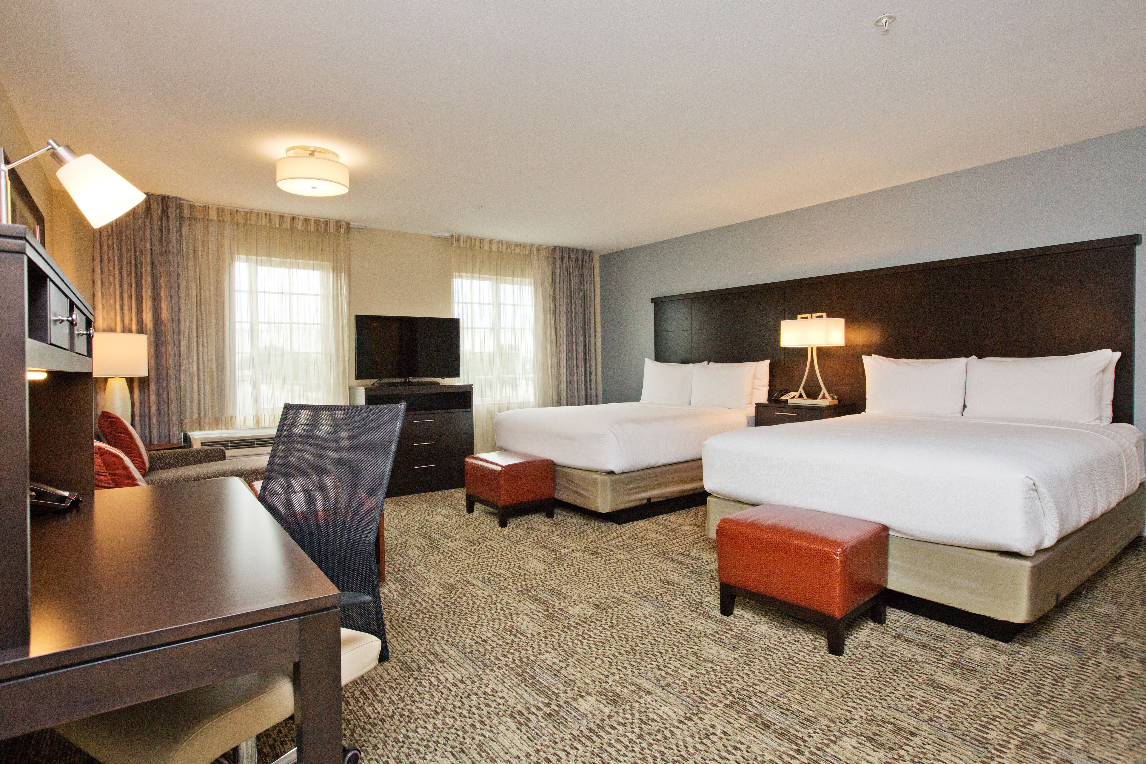 A hotel room with two beds, a desk, a chair, a television, and a lamp.