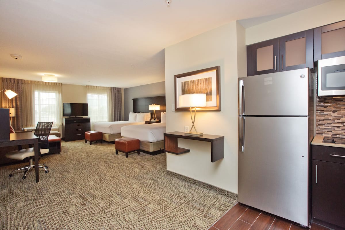 Habitación de hotel con cama, escritorio, silla y kitchenette que incluye refrigerador y microondas.