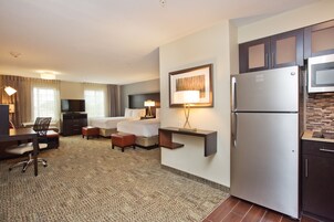 A hotel room with a bed, desk, chair, and kitchenette including a refrigerator and microwave.