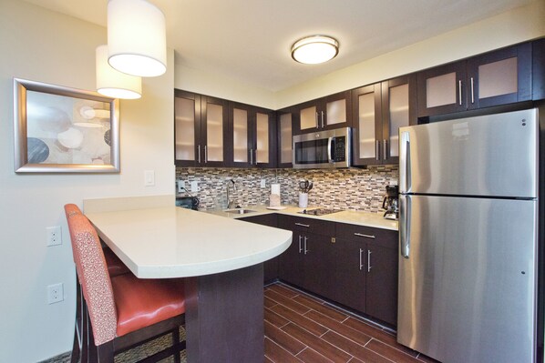 A modern kitchen with dark cabinets, stainless steel appliances, a white countertop, and a patterned chair. - Staybridge Suites Austin South Interstate Hwy 35 by IHG (Austin)