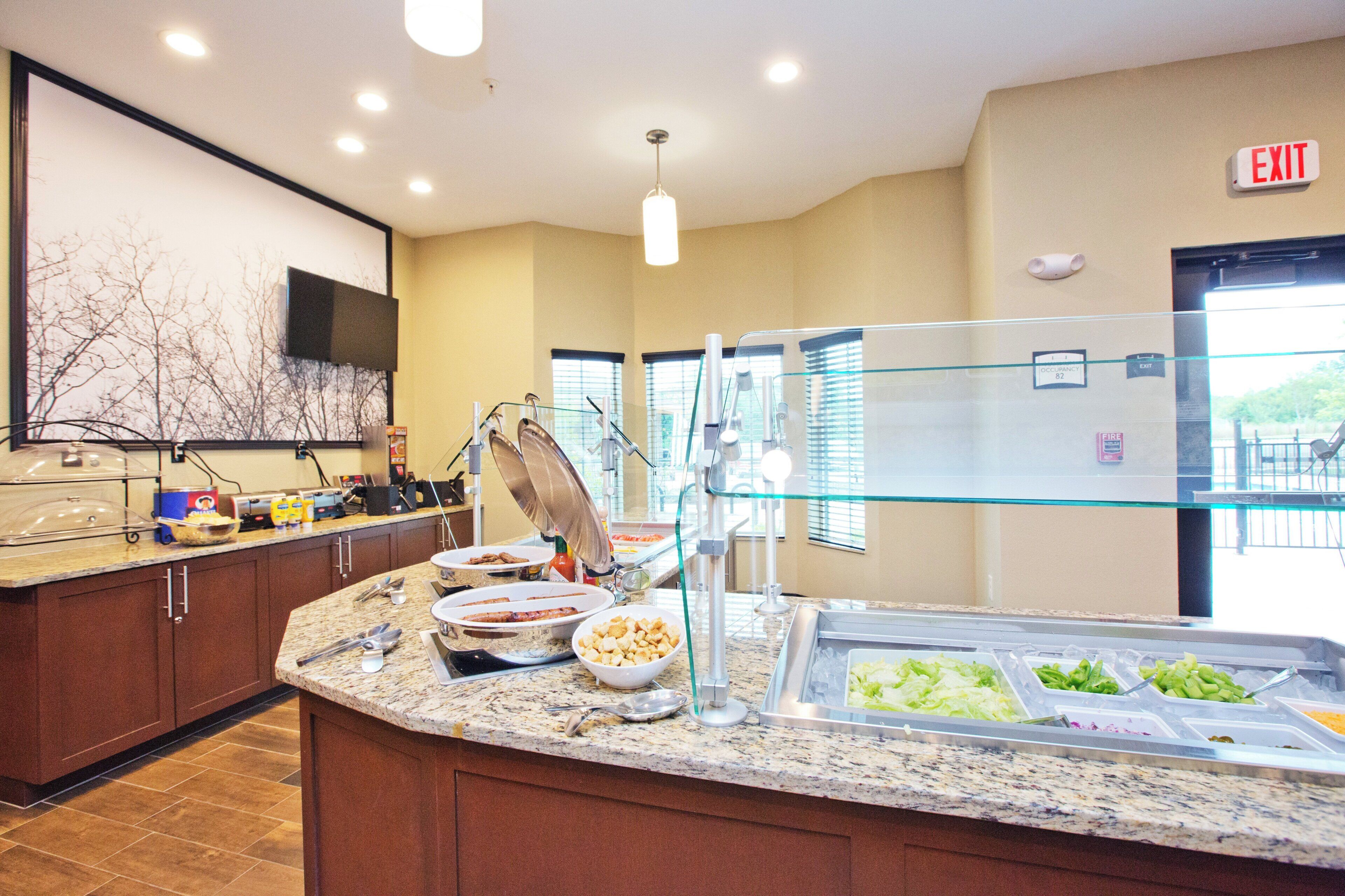 A buffet area with various food items, a glass partition, and an exit sign.