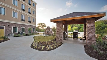 A covered outdoor seating area with stone pillars, a barbecue grill, and a patio with a landscaped garden.