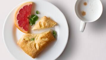 Un piatto con due pasticcini e una fetta di pompelmo, e una tazza di caffè su una superficie bianca.