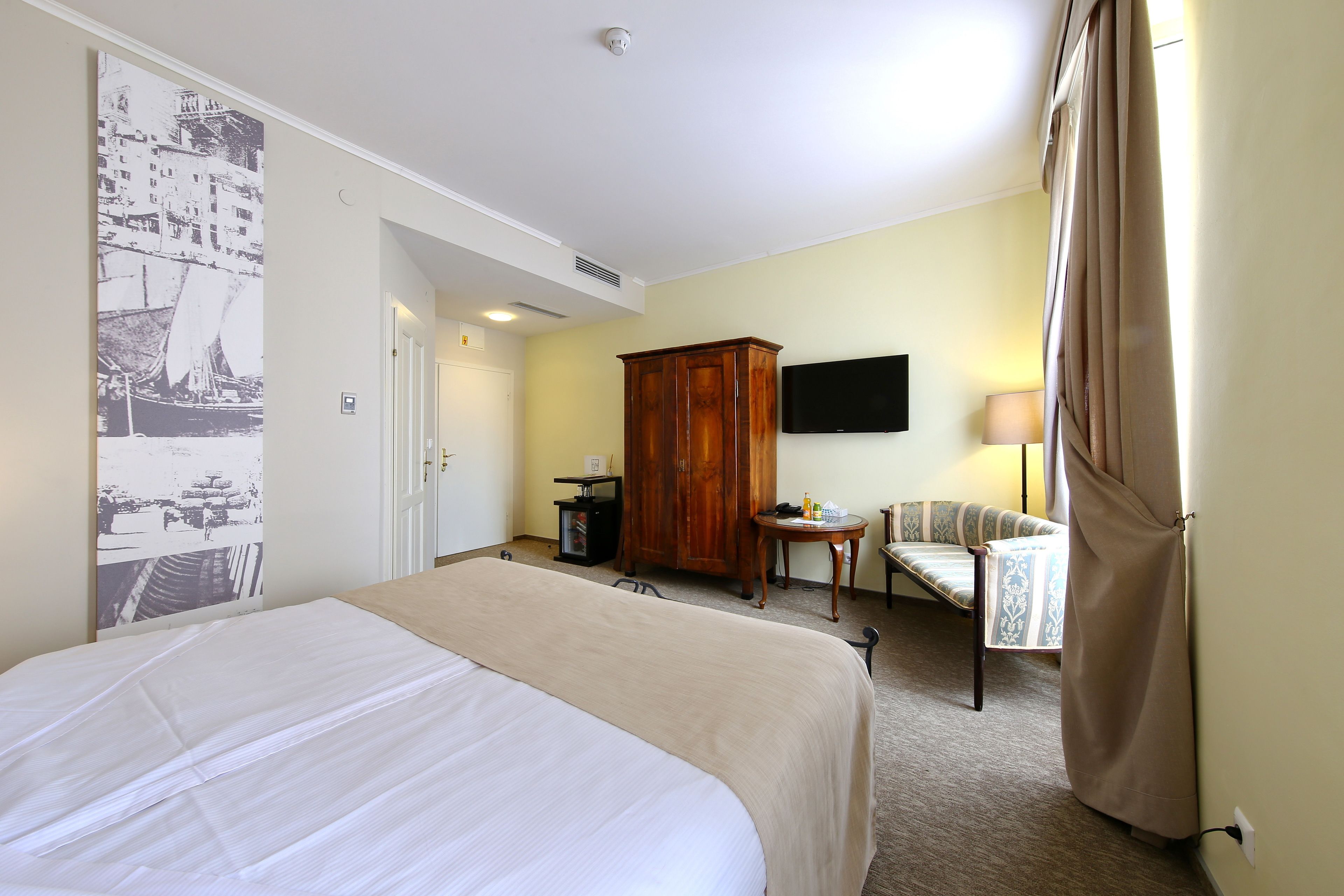 A hotel room with a large bed, a wooden wardrobe, a television, a small table with a lamp, and a chair.