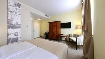 A hotel room with a large bed, a wooden wardrobe, a television, a small table with a lamp, and a chair.