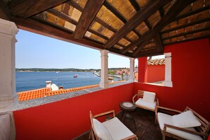 A balcony with a view of the sea, wooden chairs, and a red wall. - Angelo d'Oro Heritage Hotel (Rovinj)