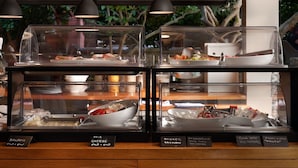 Een buffetgedeelte met verschillende gerechten, waaronder sushi, kaas, gerookte zalm, tonijn met rode paprika en verse kaas.
