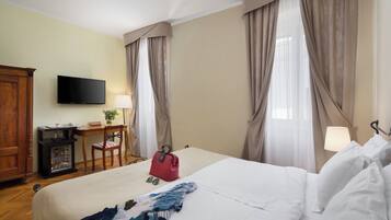 Hotellihuone, jossa on sänky, työpöytä, televisio ja verhot.