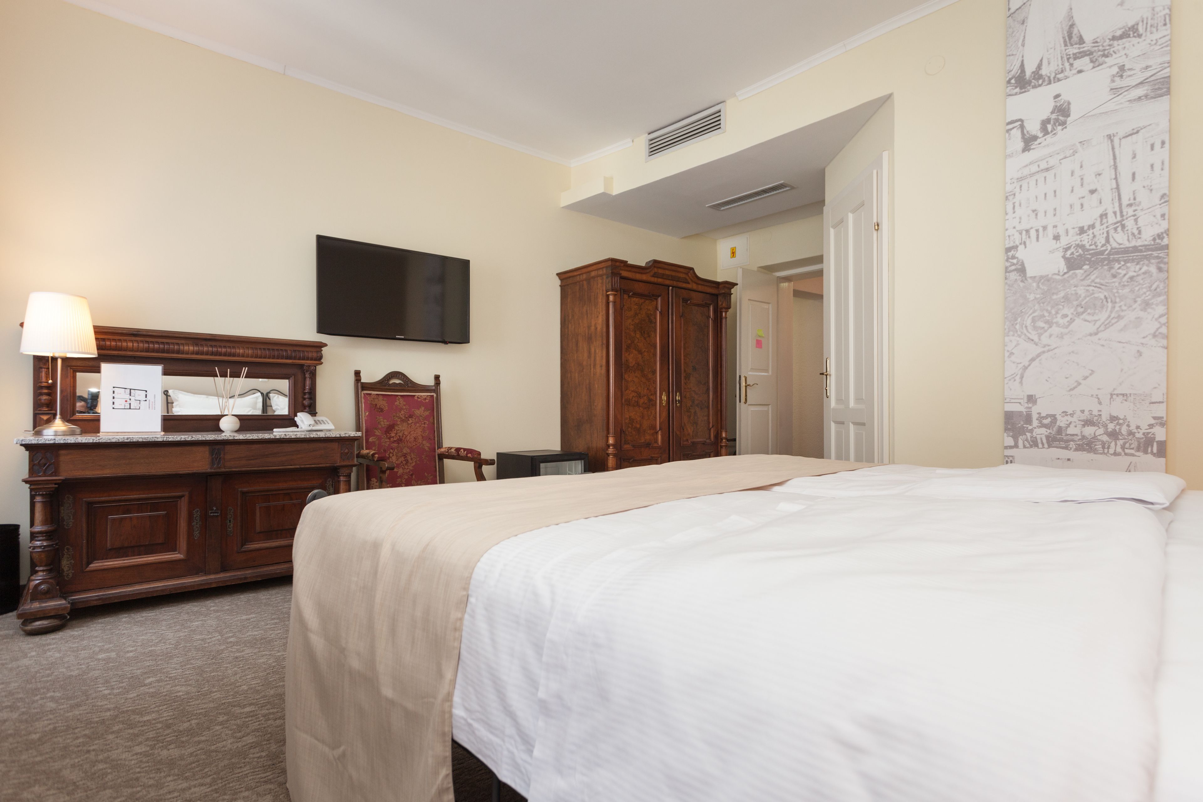 A hotel room with a large bed, a wooden dresser, a flat-screen TV, and a wall-mounted air conditioning unit.