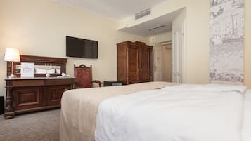 A hotel room with a large bed, a wooden dresser, a flat-screen TV, and a wall-mounted air conditioning unit.