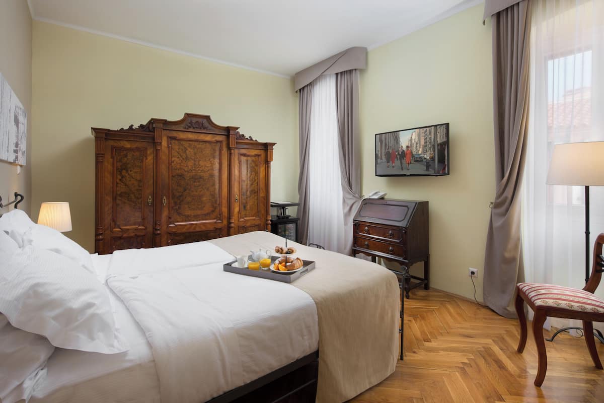 Ein Hotelzimmer mit einem großen Bett, einem Holzschrank, einem Schreibtisch mit Lampe, einem Sessel und einem Bild an der Wand.