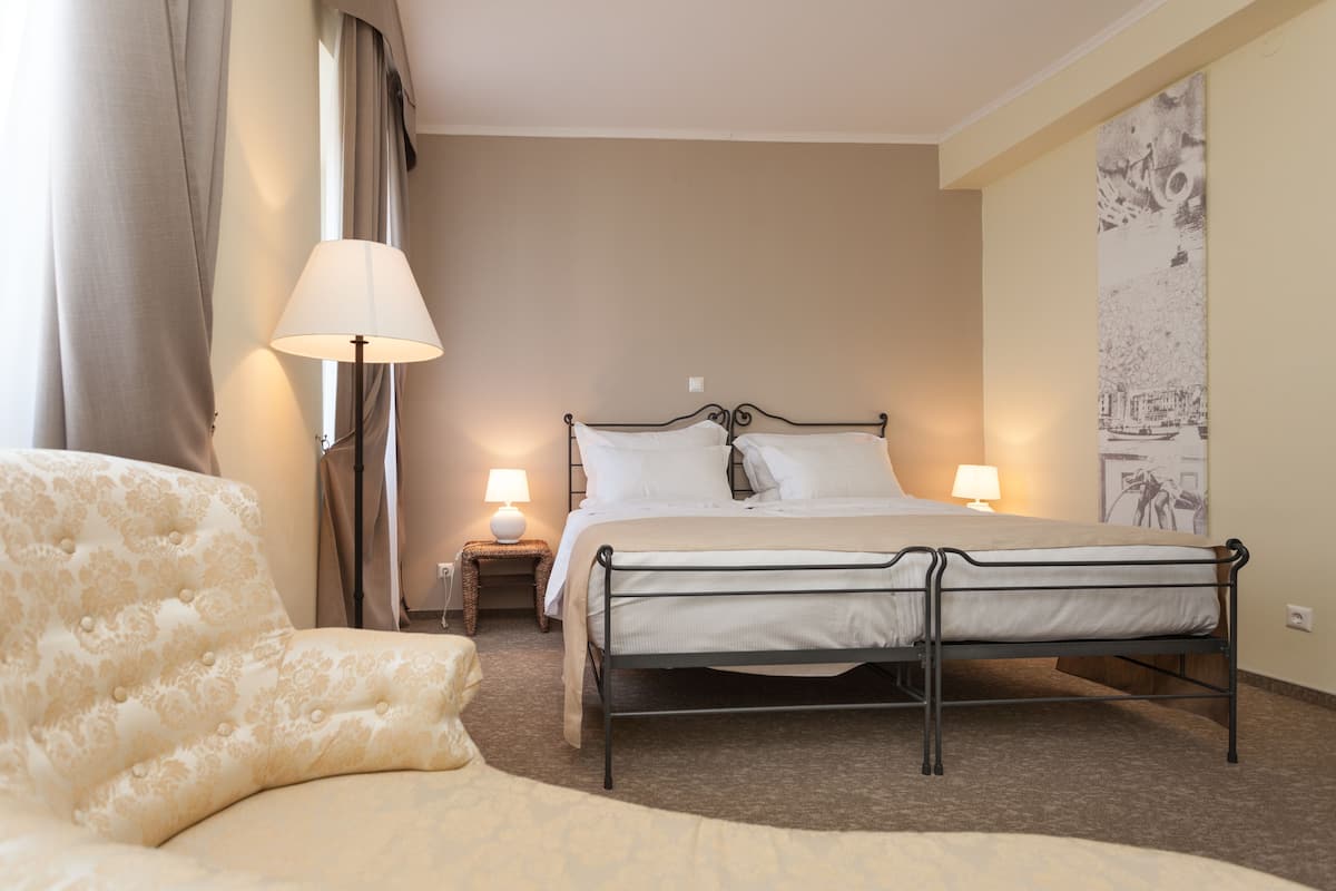 Ein Hotelzimmer mit einem Bett, Nachttischlampen, einem Sessel und einer Wand mit einem Gemälde.