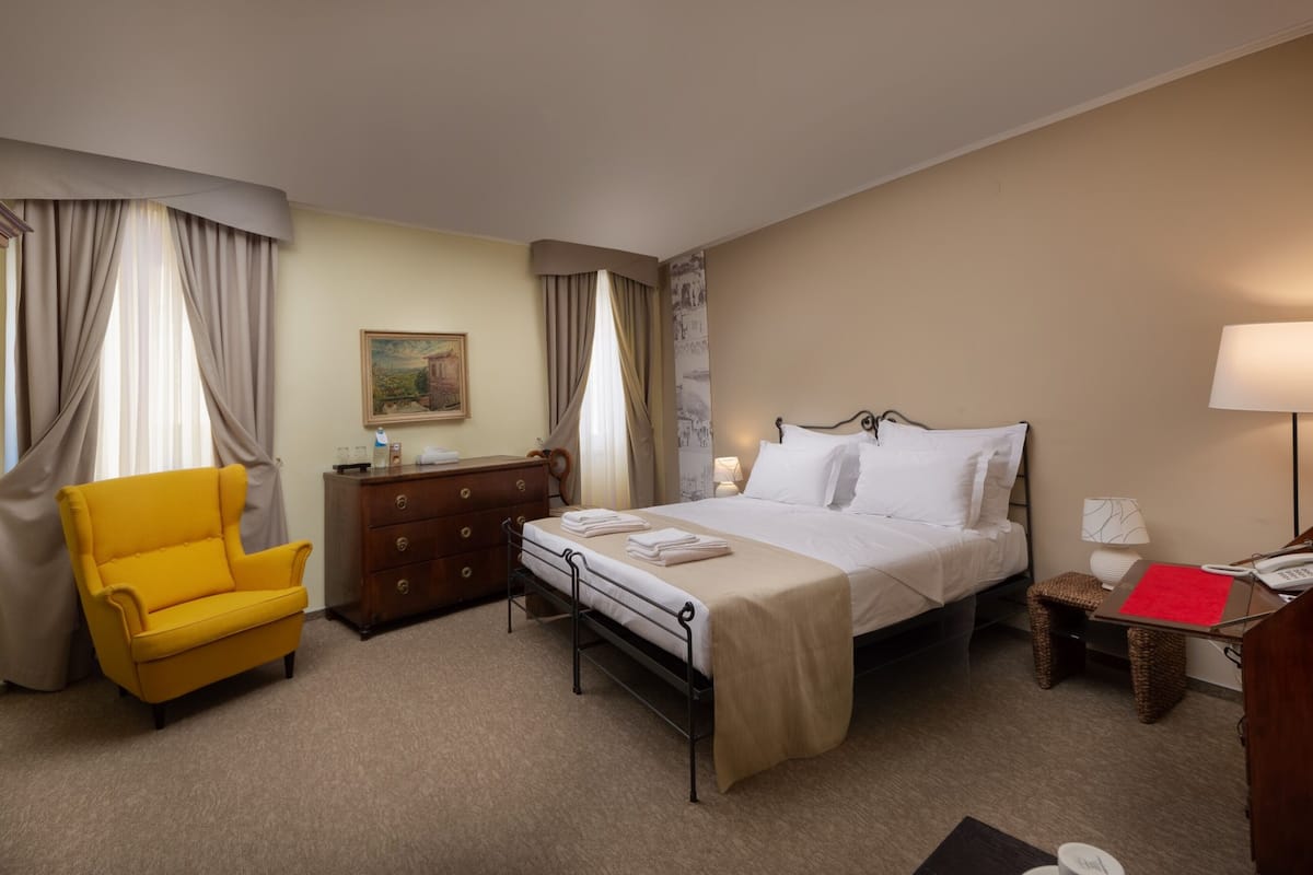 Ein Hotelzimmer mit Bett, Sessel, Kommode, Lampe und einem Bild an der Wand.