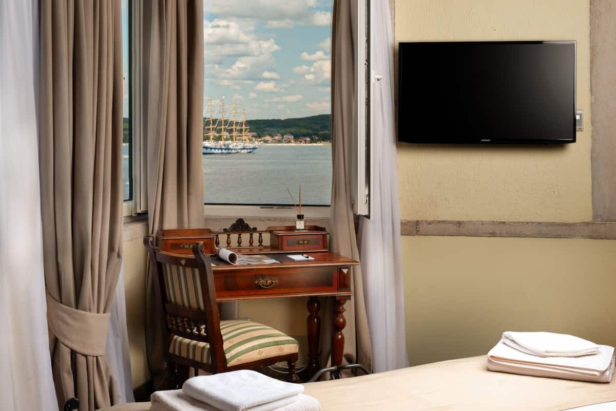 Ein Hotelzimmer mit Bett, Schreibtisch, Stuhl, Fernseher und Meerblick.
