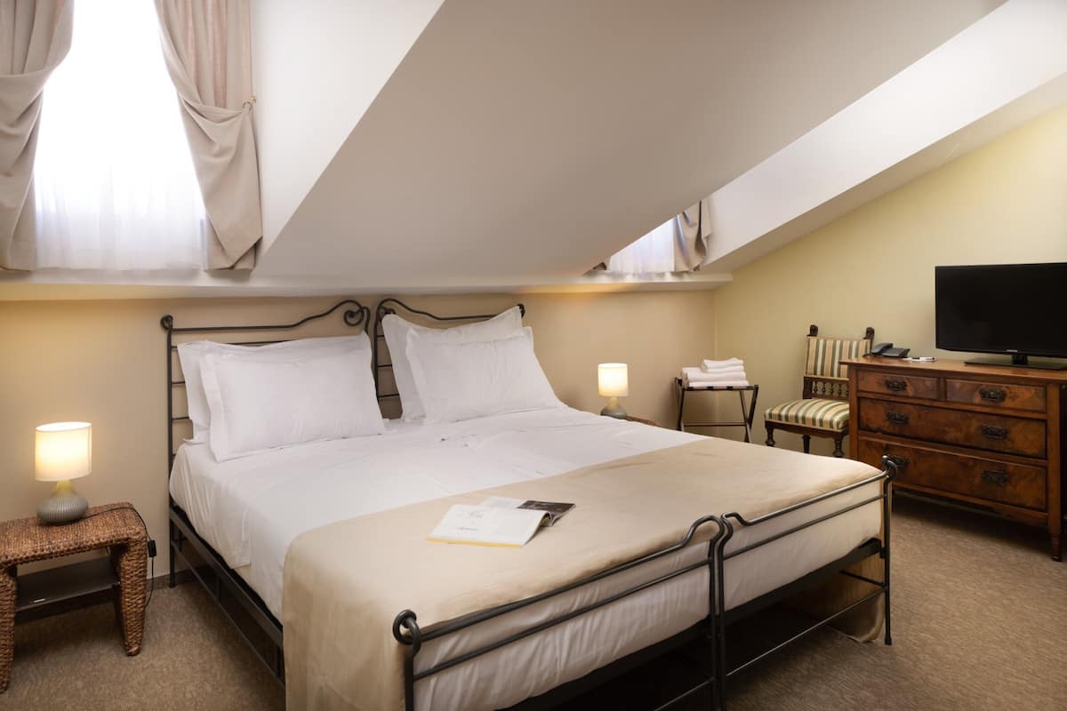 Ein ordentlich eingerichtetes Hotelzimmer mit einem Bett, Nachttischlampen, einer Holzkombination, einem Fernseher und einem Fenster mit Vorhängen.
