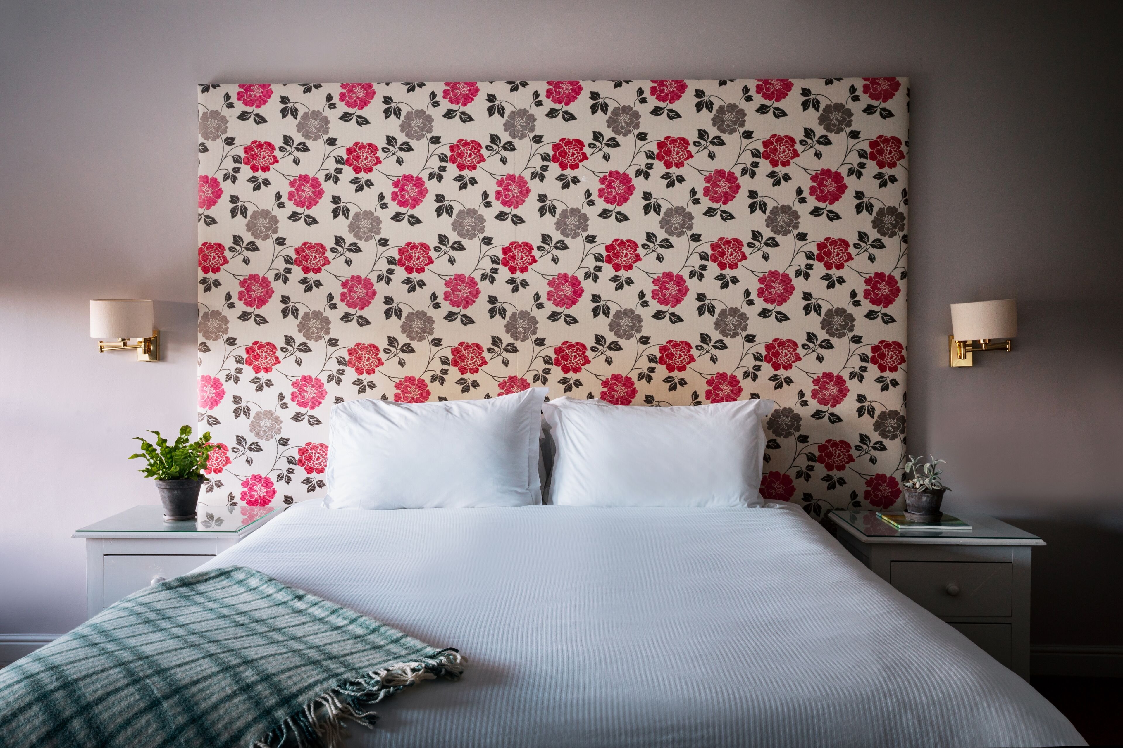 A neatly made bed with white linens, a floral-patterned headboard, and two bedside lamps.