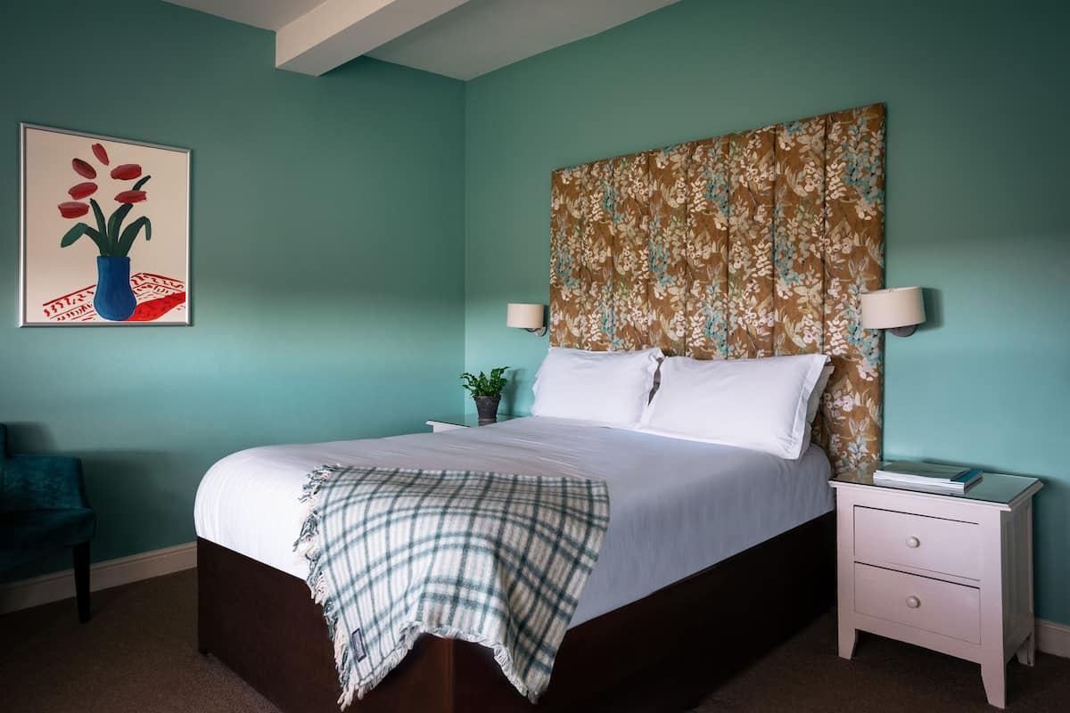 A bedroom with a bed, nightstand, lamp, and a painting on the wall.