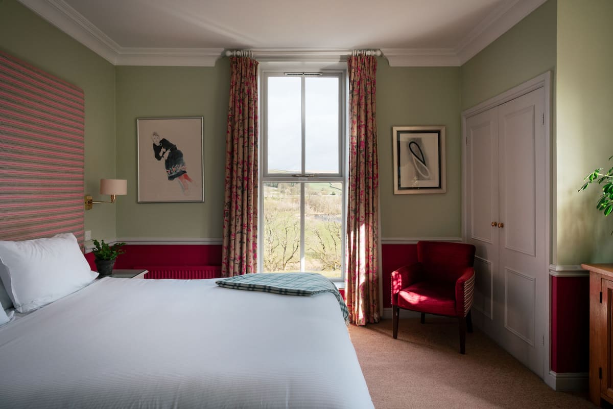 A bedroom with a large bed, a red chair, a window with curtains, and a door.