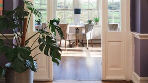 A room with a wooden floor, a dining table with chairs, and a view of the outdoors through large windows. - The Fell Hotel (Skipton)