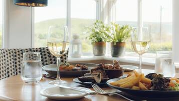 Uma mesa de jantar com pratos de comida, copos de água e vinho, e vista para o exterior.