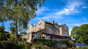 A historic stone building with a pub on the ground floor, surrounded by well-maintained gardens and a clear blue sky. - The Fell Hotel (Skipton)