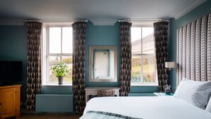 A bedroom with a large bed, a window with curtains, a radiator, a television, and a plant. - The Fell Hotel (Skipton)