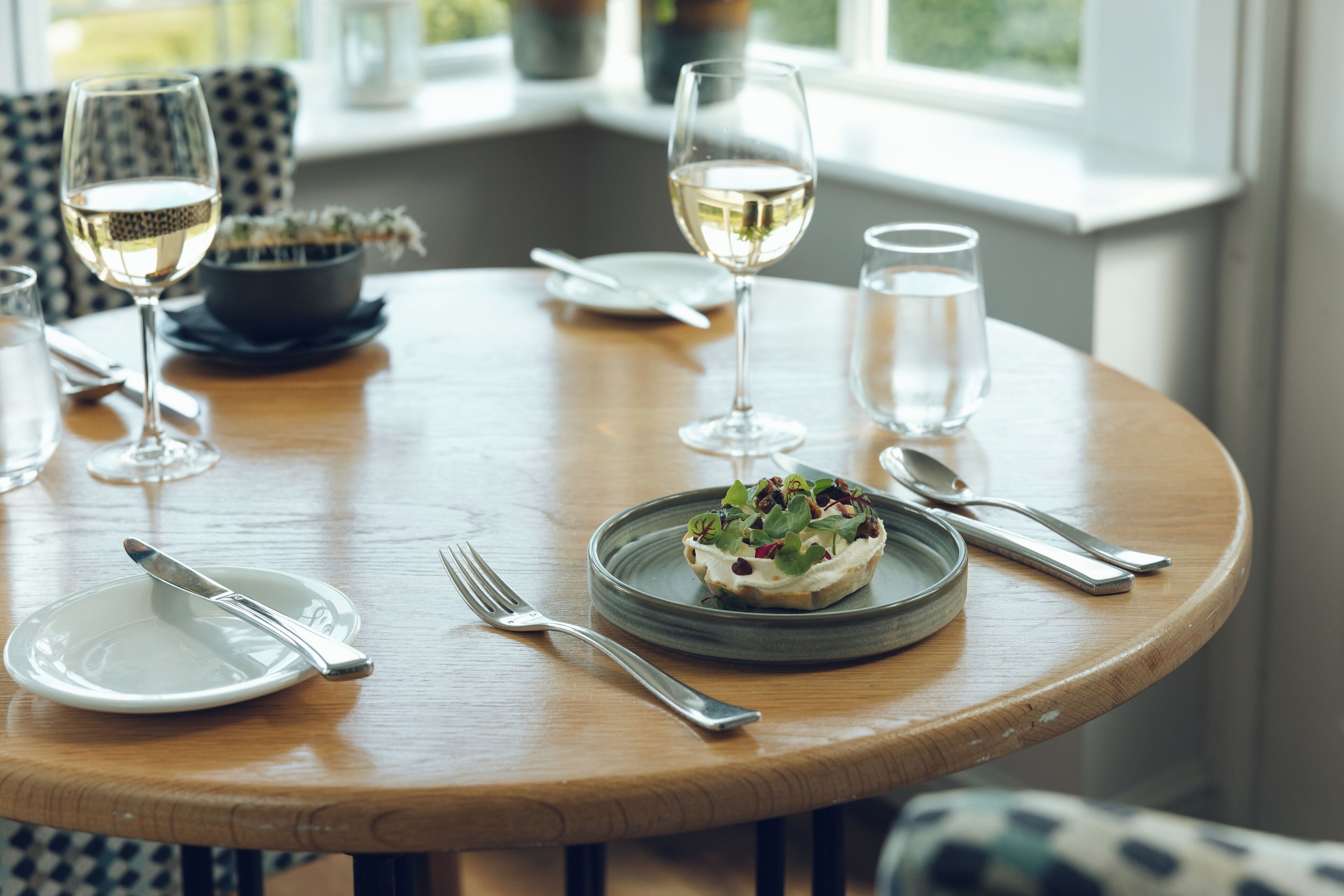 A dining table set with plates, cutlery, glasses, and a bowl of salad.