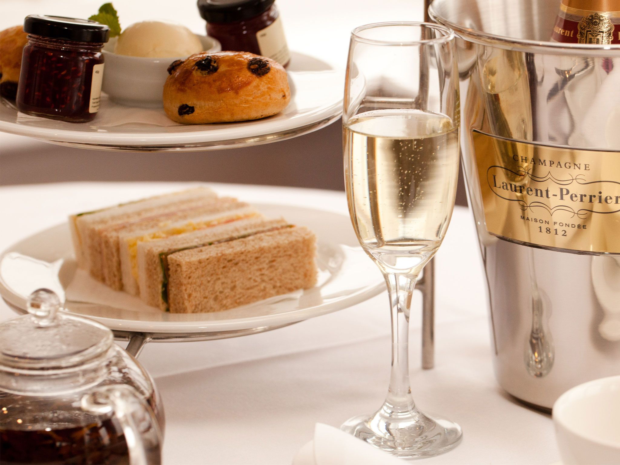 A table setting with sandwiches, a glass of champagne, and a bottle of Laurent-Perrier champagne.