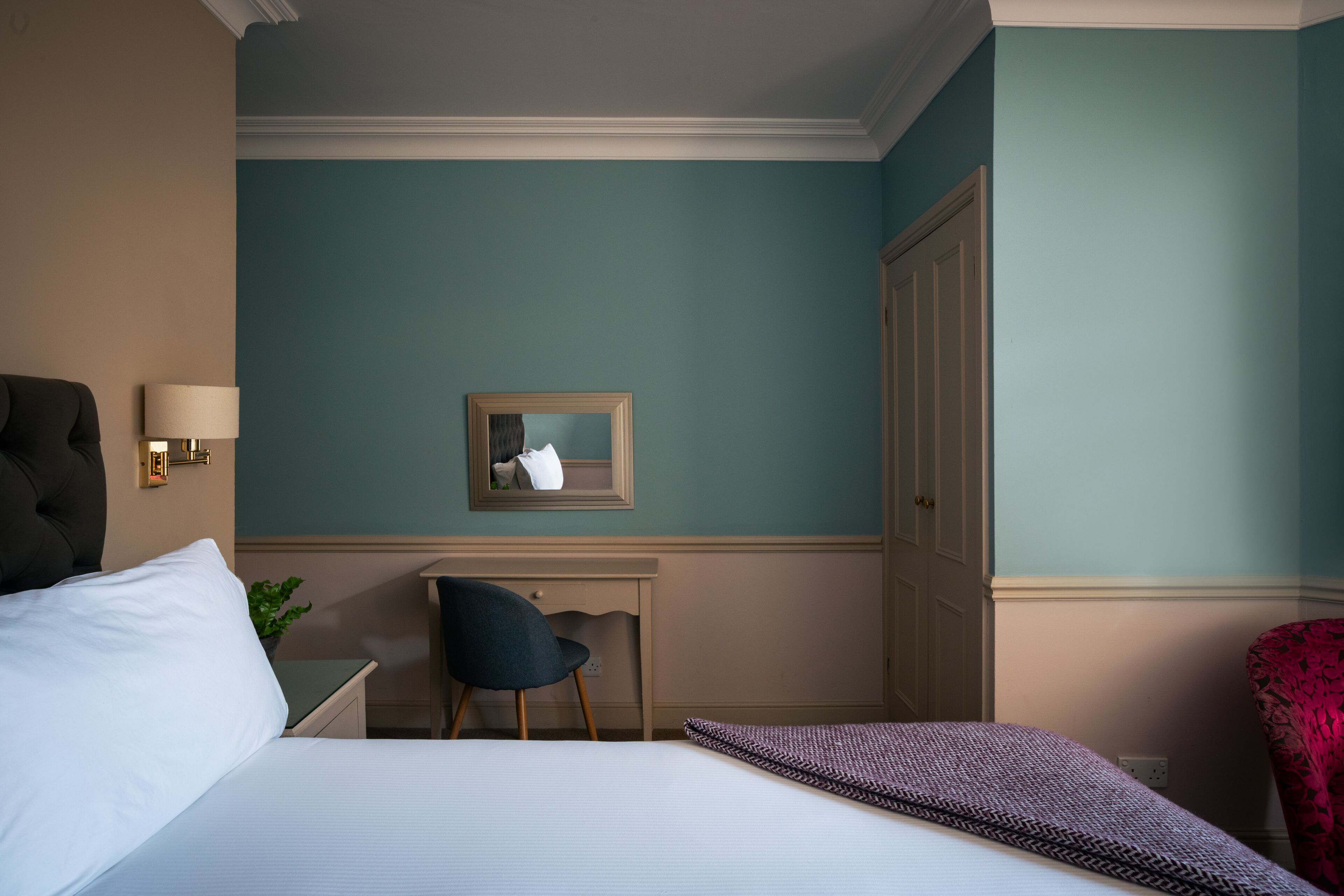 A hotel room with a bed, a desk, a chair, a wardrobe, and a mirror on the wall.