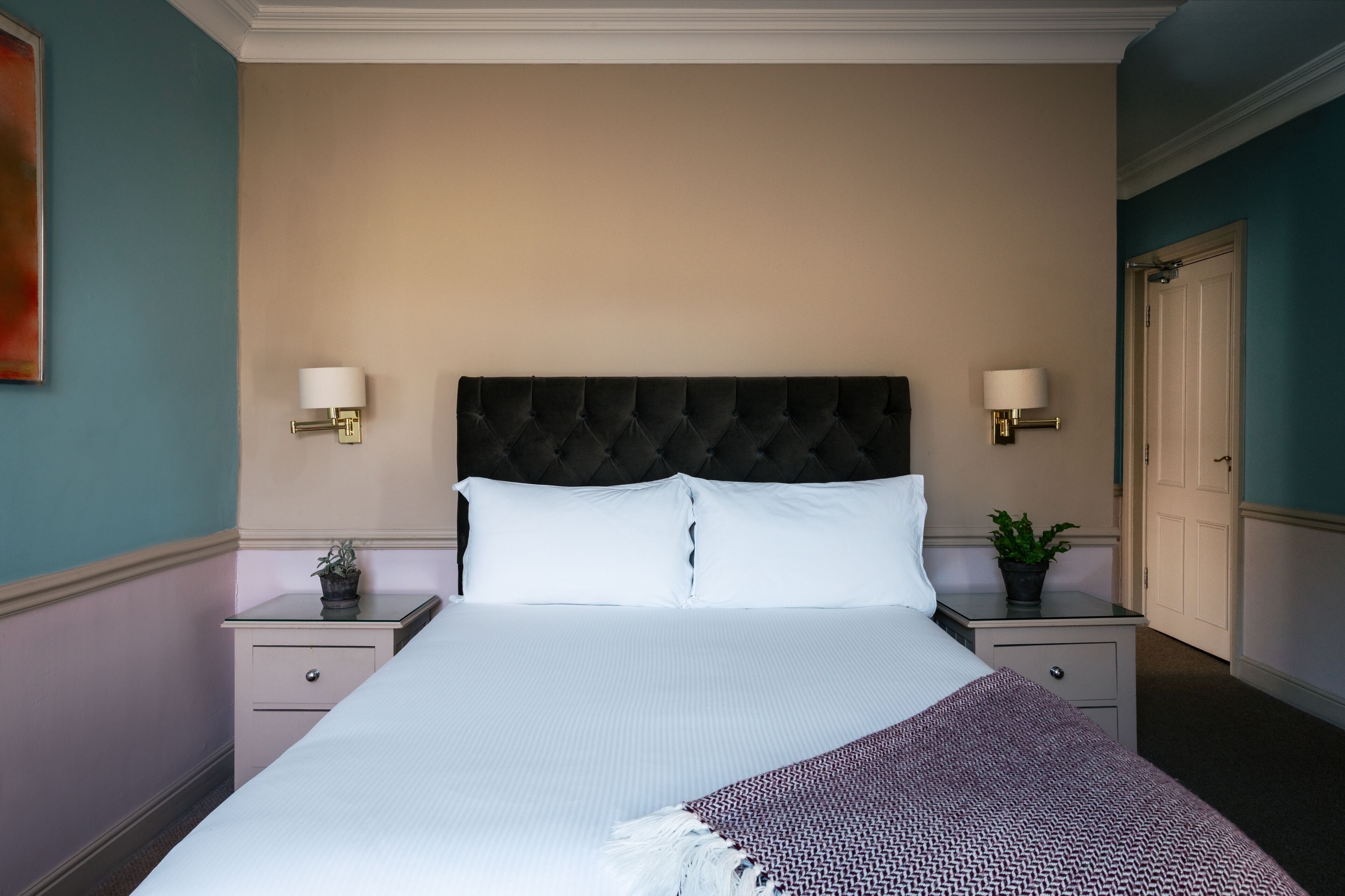 A neatly made bed with a tufted headboard, two bedside lamps, and a bedside table with a plant.