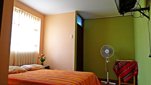 Una habitación con cama, ventilador y ventana con cortinas.