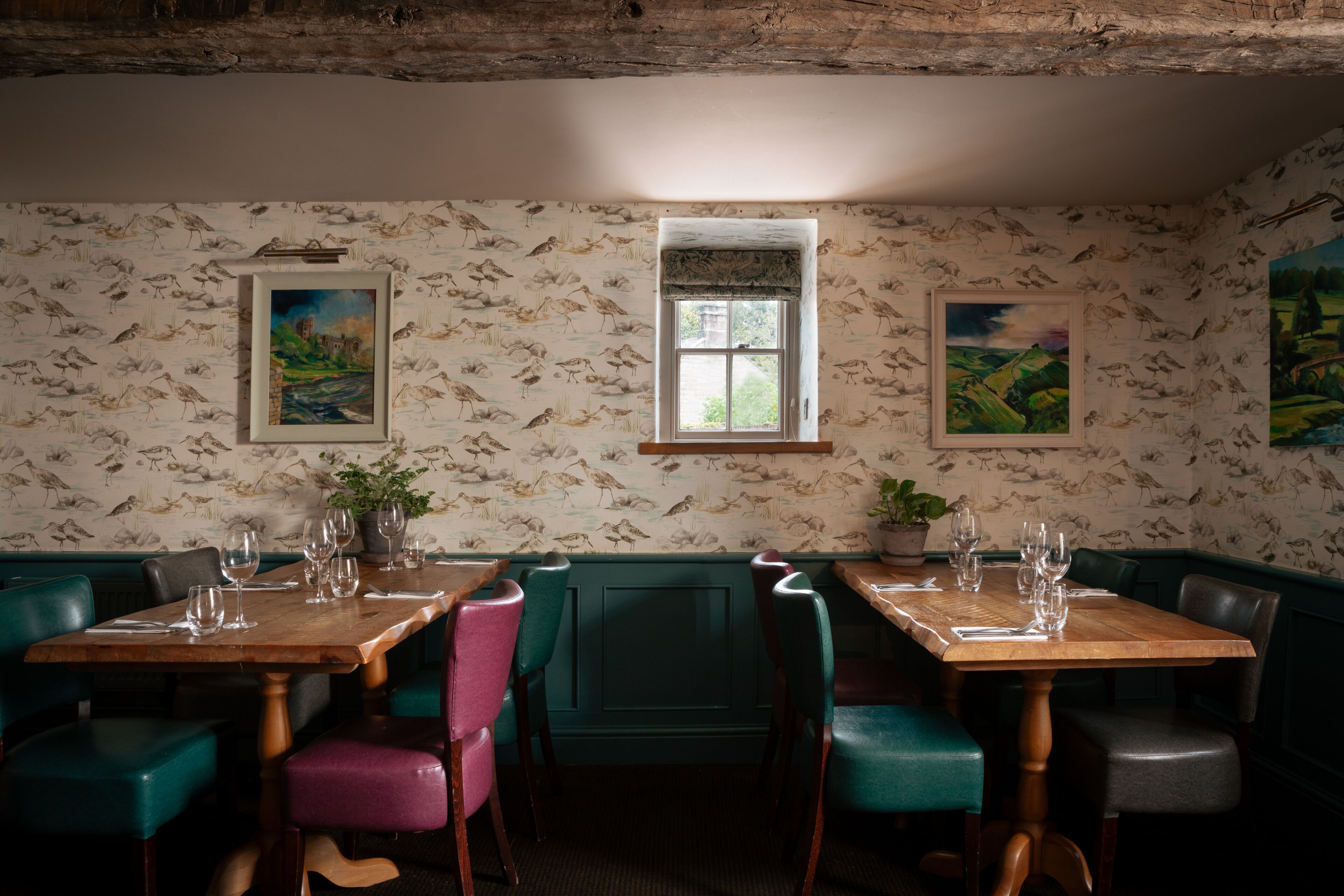 A dining area with a wooden table, green and pink chairs, and a window with a view.