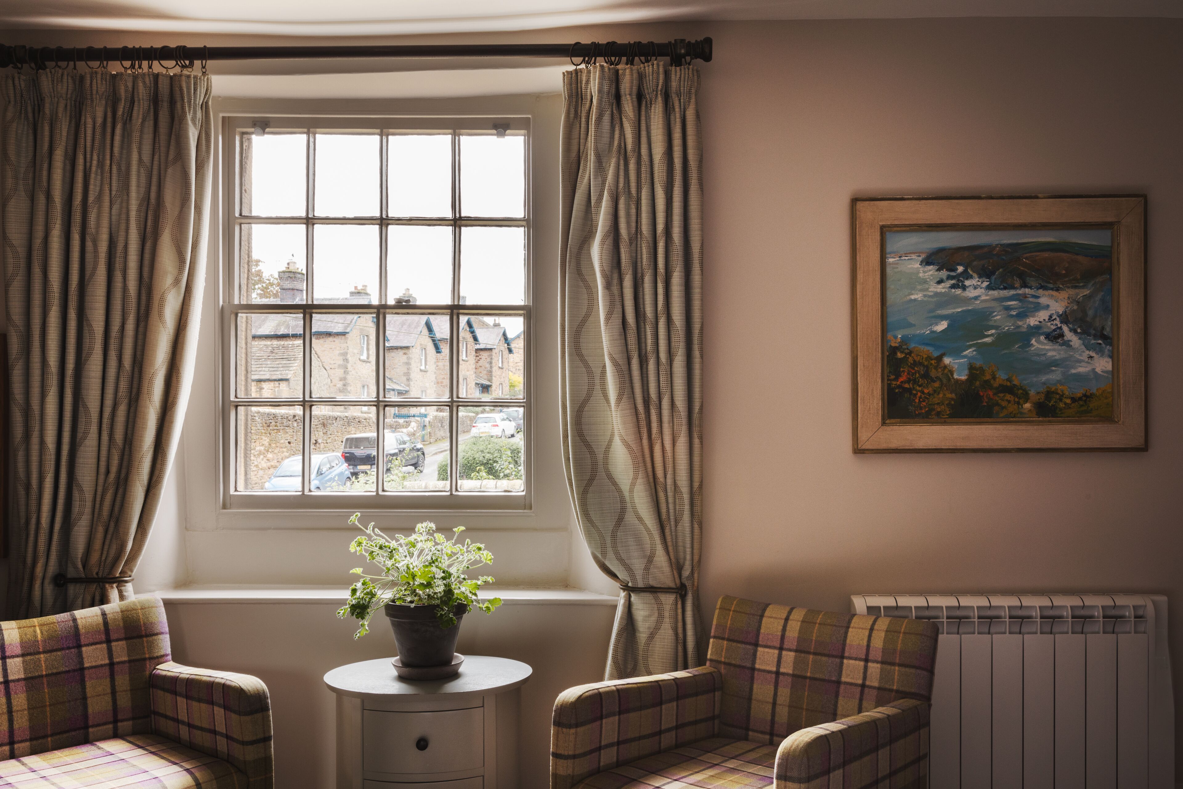 A room with a window, a radiator, a painting, and two plaid chairs.