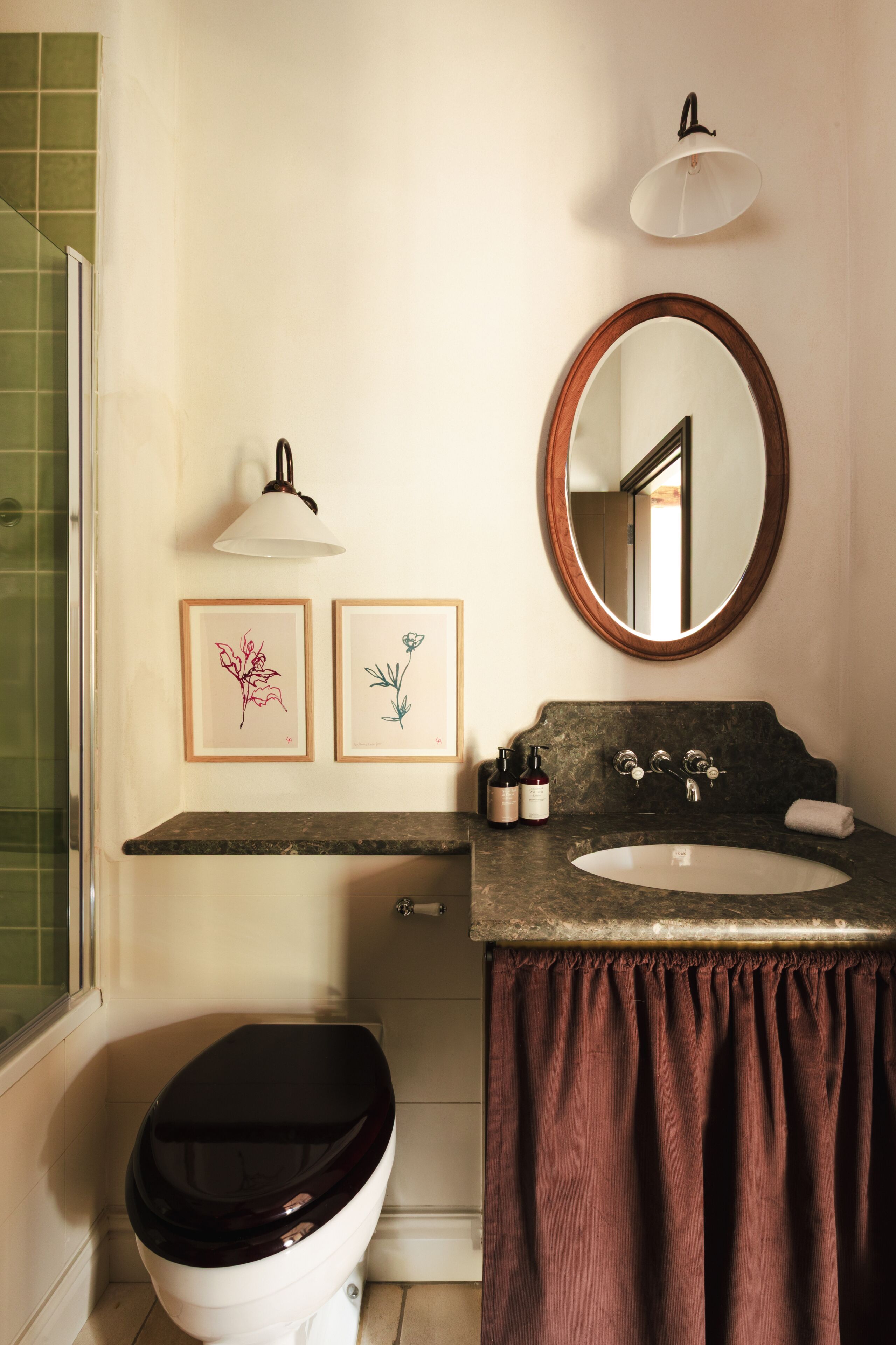 A bathroom with a toilet, sink, framed artwork, and a mirror.