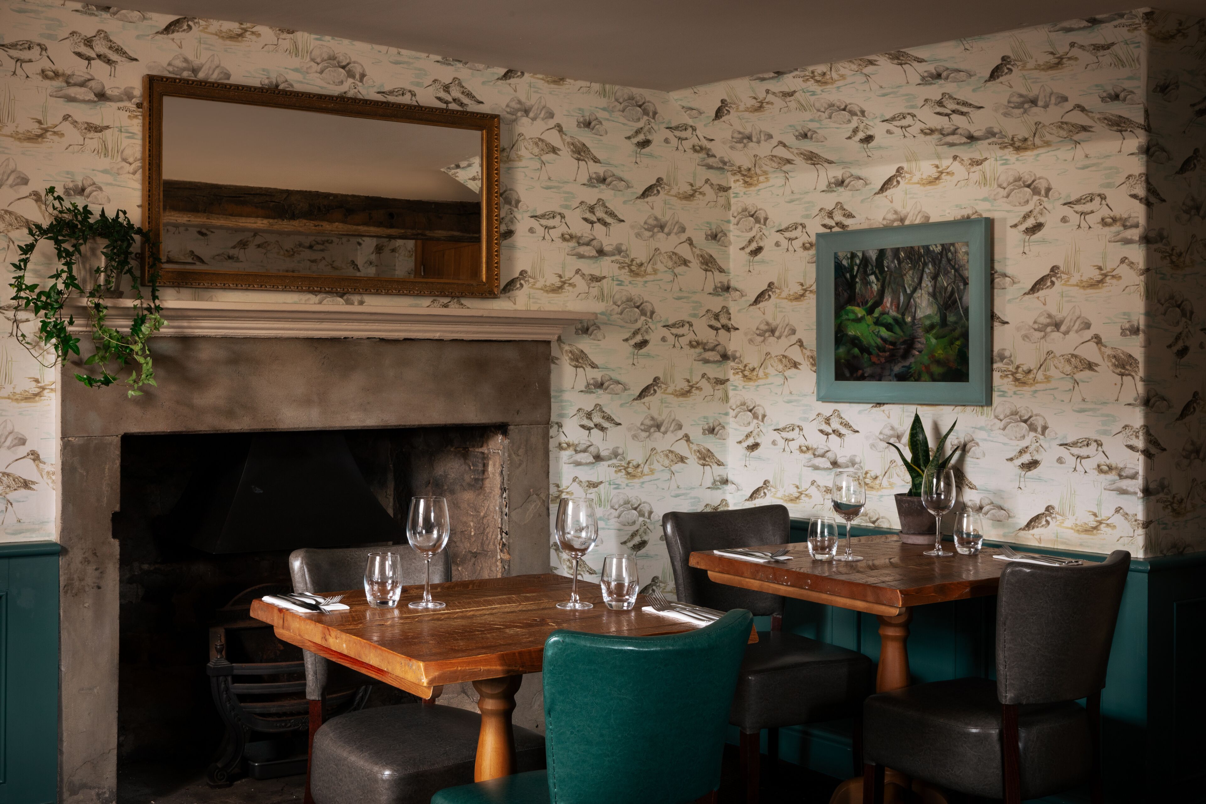 A dining area with a fireplace, a mirror, and a wall with bird wallpaper.